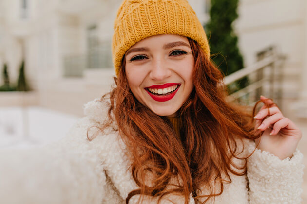年轻可爱的欧洲女士在享受冬天穿着白大褂的姜黄色女孩在户外自拍街道兴奋女模特
