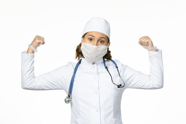 疾病正面图年轻女医生戴着无菌口罩和手套 因为冠状病毒在白色表面弯曲听诊器医疗护士
