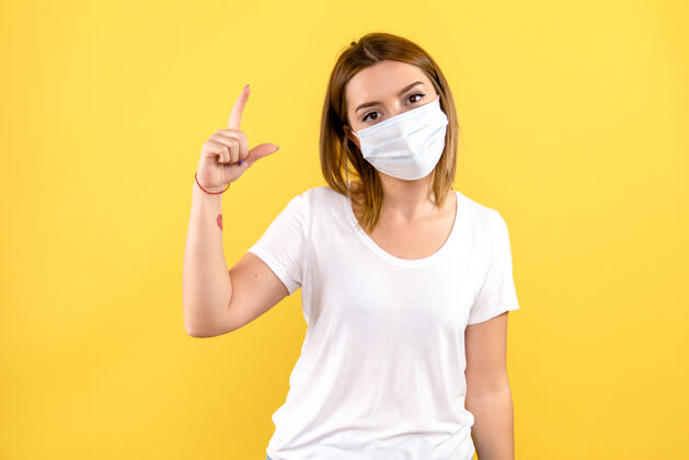 病毒黄色墙壁上戴着无菌口罩的年轻女子的正视图护士年轻女性健康