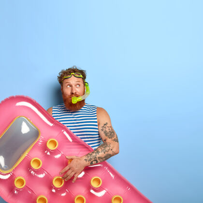 护目镜体贴的红发男人戴着潜水面罩 喜欢游泳和休息 拿着粉色充气床垫的垂直镜头休闲白种人红发