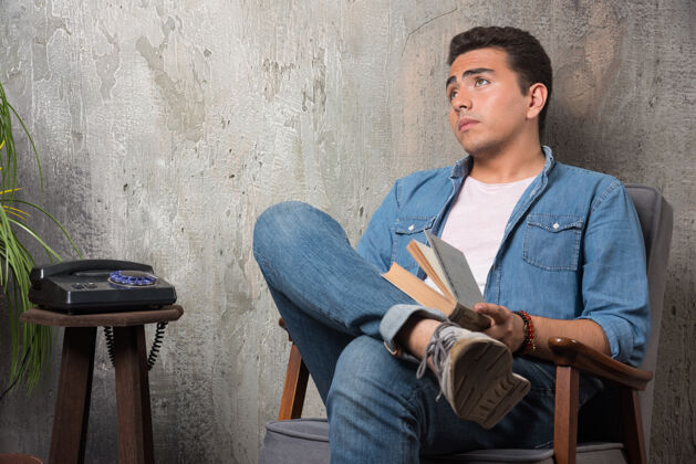 年轻人年轻人拿着书抬头 坐在大理石背景的椅子上高质量的照片小伙子男人电话