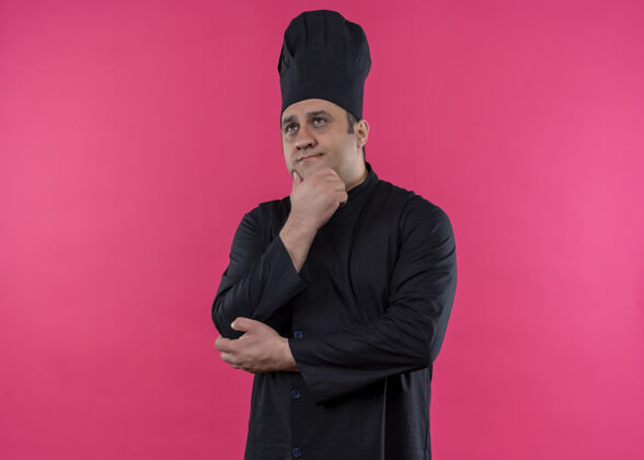 看男厨师身穿黑色制服 头戴厨师帽 手放在下巴上 面带沉思的表情 站在粉色背景上制服烹饪站