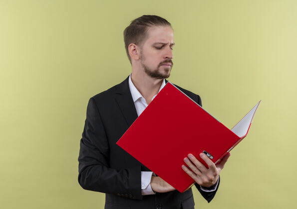 男人穿着西装的帅哥拿着红色的文件夹看着它 严肃的脸站在绿色的背景上穿脸立场