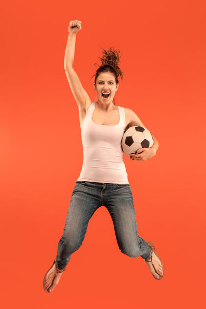 球迷前进的胜利年轻女子作为足球运动员跳跃和踢在工作室的红色背景球足球迷和世界冠军的概念人类情感的概念足球冠军成人