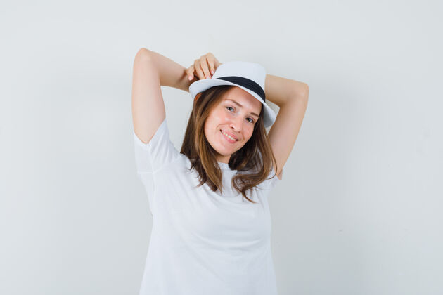 放松年轻女子举着双手 头后穿着白色t恤 戴着帽子 看上去很放松期待脸提高