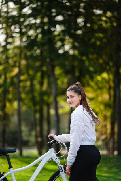 女人美丽的女孩在白色自行车前摆姿势在大自然中漫步漂亮自行车自然