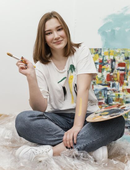 画布一个年轻女子在她的彩画旁摆姿势绘画室内室内