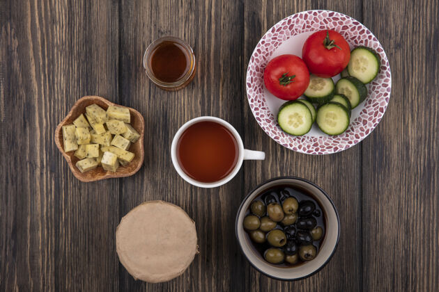 顶部一碗新鲜橄榄的顶视图 一杯茶 蔬菜和切碎的奶酪片放在木制背景上茶新鲜视野