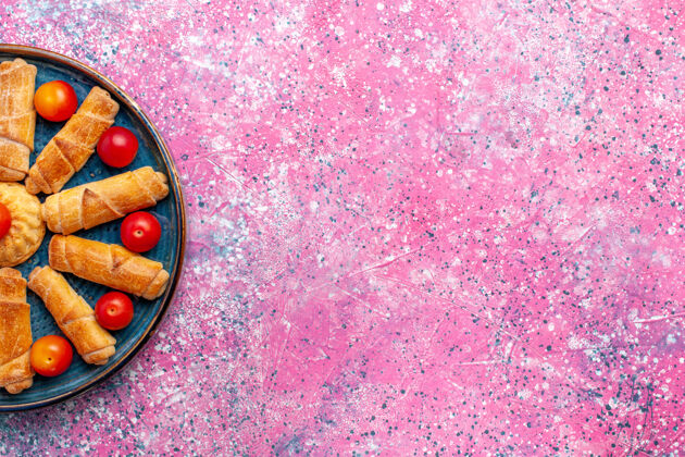糕点顶视图甜美美味的百吉饼烤糕点托盘内与李子在淡粉色的办公桌上手镯桌子饼干