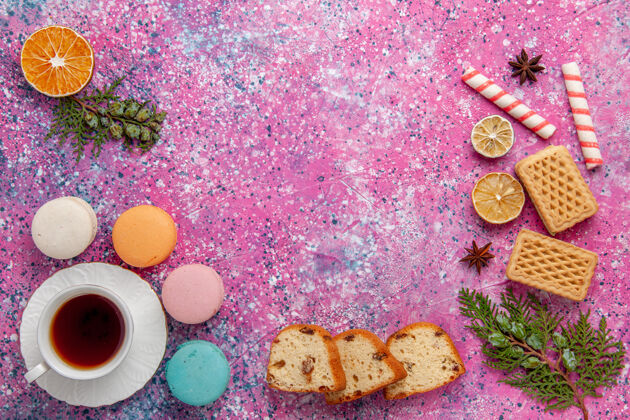 法国顶视一杯茶与法国马卡龙和华夫饼在粉红色的表面麦卡龙生的模式