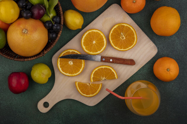 绿色顶视图用刀在砧板上切橘子片葡萄柚柠檬李子和桃子放在绿色背景的篮子里酸橙新鲜顶部