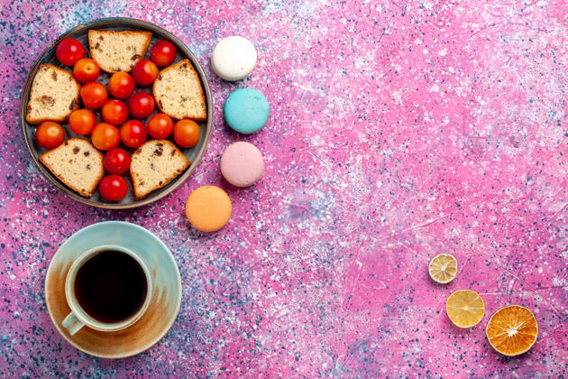 新鲜的俯瞰美味的切片蛋糕与酸新鲜李子麦卡龙和一杯茶在粉红色的表面馅饼切片球