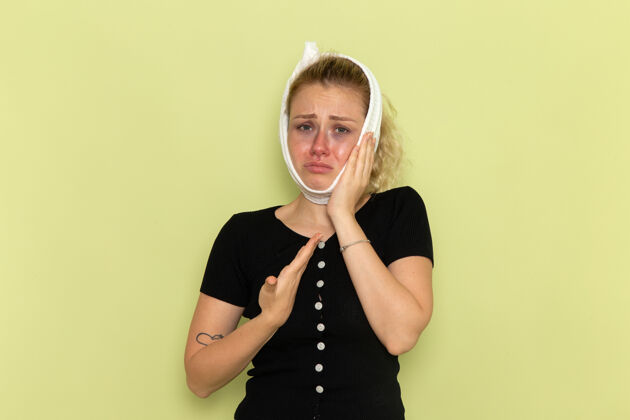 肖像正面图年轻女性 头上围着白毛巾 感觉很不舒服 绿色墙壁上牙痛生病生病女性健康感情视图周围