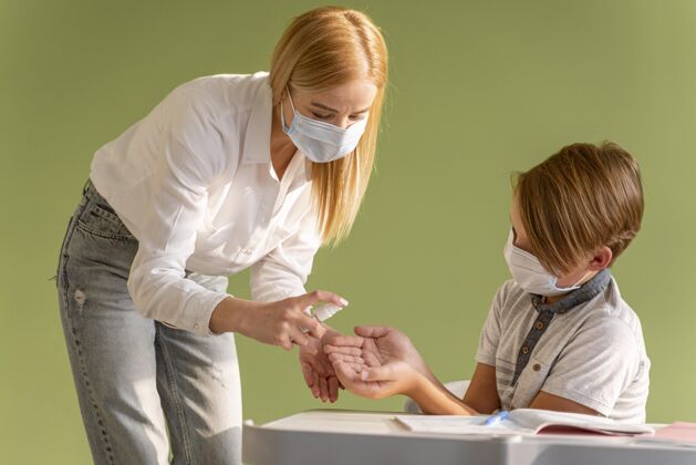 新常态老师带着医用面罩在课堂上给孩子的手消毒的正面图面罩返校学生