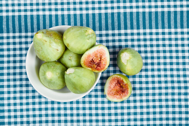 切片绿色的无花果放在一个白色的碗里 放在一张铺着蓝色桌布的木桌上美味桌布水果