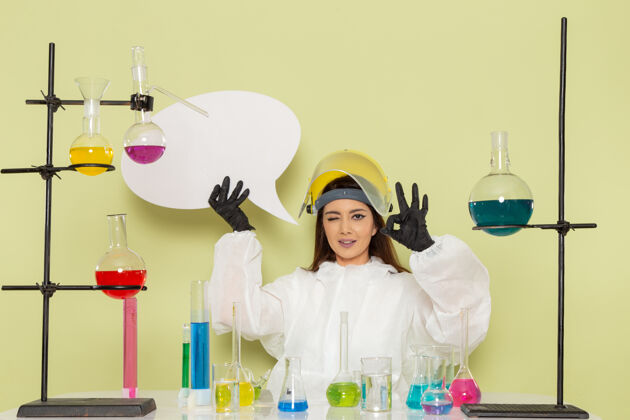 科学正面图身着特殊防护服的年轻女化学家手持巨大的标牌在绿色墙上化学工作女科学实验室观点西装化学家
