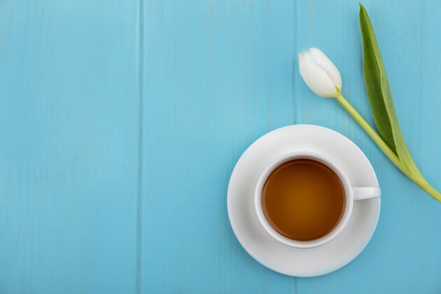 视图茶碟上的茶杯和蓝色背景上的花朵顶视图 带有复制空间蓝色桌子茶