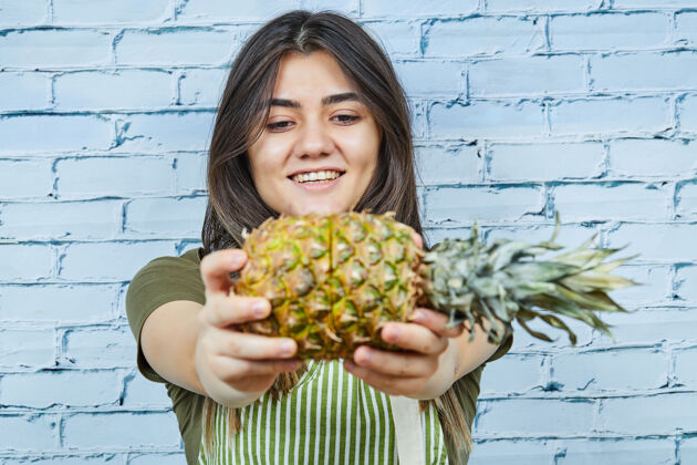 热带快乐的年轻女子拿着菠萝在蓝色的表面有机成熟菠萝