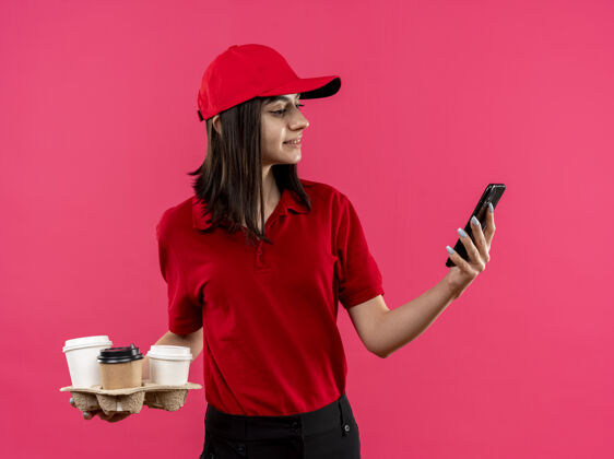 抱着年轻的送货员穿着红色马球衫 戴着帽子 手里拿着食品包 在粉红色的墙上晃来晃去戴着帽子送货