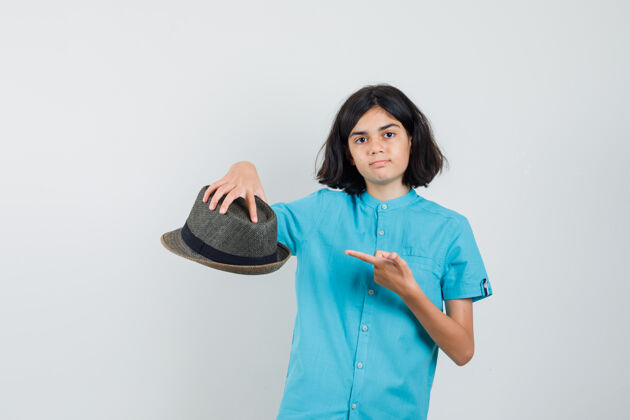 年轻年轻的女士拿着帽子指着它 穿着蓝色衬衫 看起来很专注优雅时尚蓝色