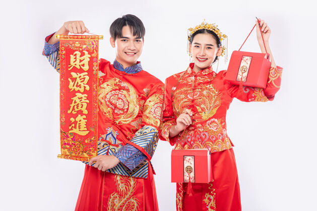 中国新年男男女女身穿旗袍站着 手持问候牌 背着红包乐趣给予男人