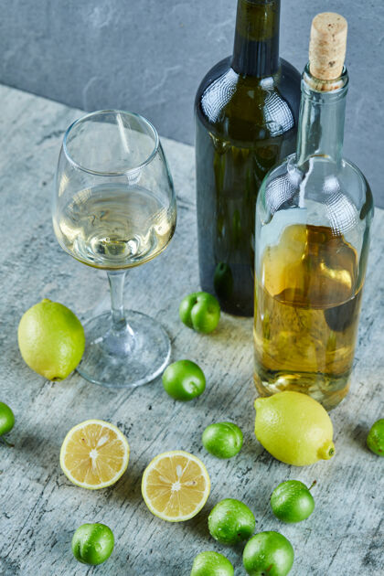 酒精两瓶和一杯葡萄酒放在大理石桌上 上面放着柠檬和樱桃李子成熟樱桃葡萄酒