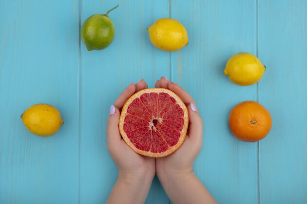 绿松石俯视图：一个女人拿着半个柚子和青绿色背景上的酸橙和柠檬顶部水果橙子