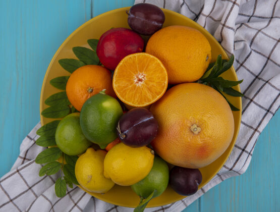 酸橙在绿松石色背景的格子毛巾上 黄色盘子上放着葡萄柚和橙子 李子 柠檬和酸橙李子柠檬毛巾