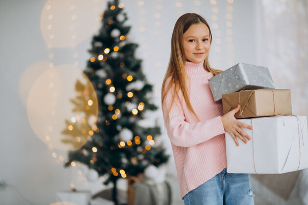 孩子可爱的女孩拿着圣诞礼物在圣诞树旁开放的礼物圣诞老人明亮