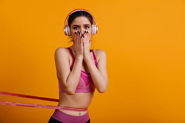 运动装戴着耳机测量腰围的可爱年轻女子运动减肥运动