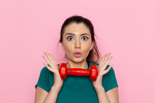 人正面图年轻女性手持红色哑铃在粉红色的墙上运动员运动锻炼健康锻炼运动员运动肖像
