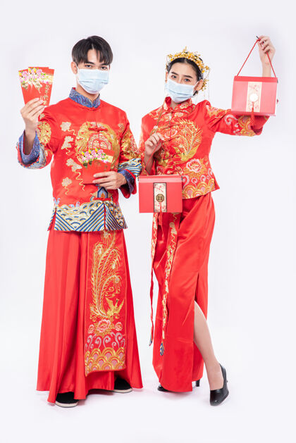 微笑男男女女戴着口罩和旗袍 手里拿着红色礼金和红包站立幸运中国民族