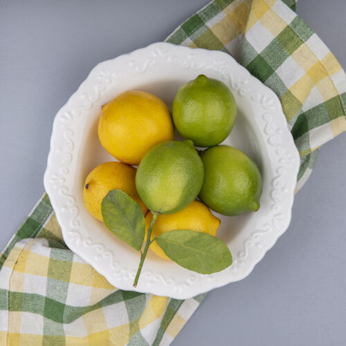 酸橙在灰色背景下 黄色格子毛巾上的盘子里放着柠檬和酸橙上衣水果黄色