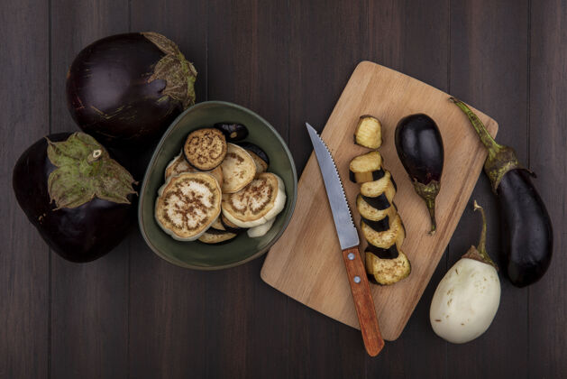 烹饪顶视图黑色茄子与楔子在一个碗和砧板上用刀在木制背景楔食物切