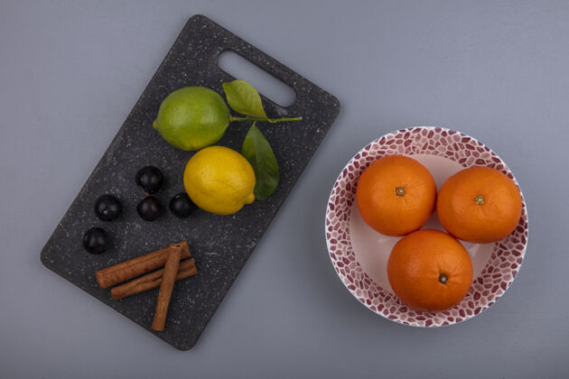 柠檬俯瞰图：柠檬 樱桃 李子和肉桂放在砧板上 橘子放在盘子里 背景是灰色的柑橘橘子切