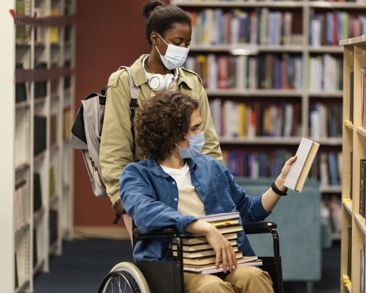 学术在图书馆里帮助坐轮椅的同事选书的女孩男人知识年轻成人