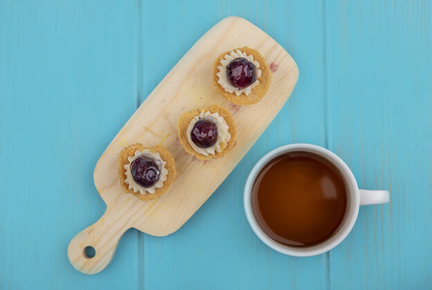 板蓝色木制背景上的木制厨房板上的一杯茶和糖果的俯视图木头蓝色茶
