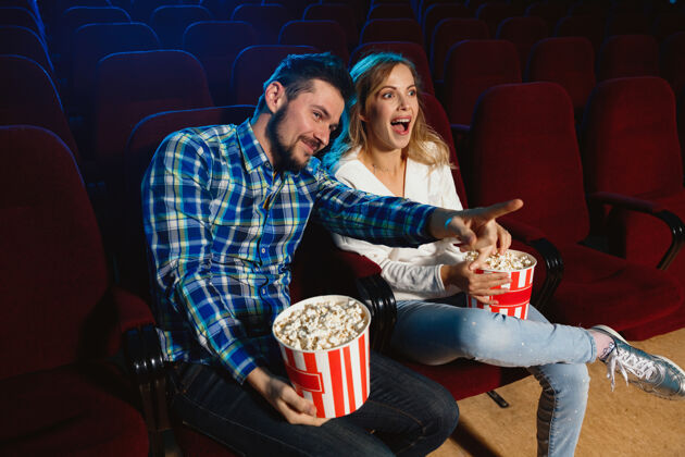 房子迷人的年轻白种人夫妇在电影院 房子或电影院看电影看起来富于表现力 惊讶和情绪化独自坐着玩关系 爱情 家庭 周末时间座位微笑年轻