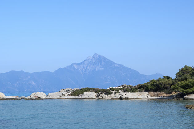 岩石爱琴海沿岸有岩石和休息的人 远处有山 前景是绿意盎然 蓝色的海水 希腊岩石镁砂海景