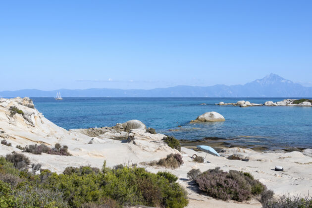 悬崖爱琴海沿岸有游泳的人 水面上有岩石 远处有船 前景是绿色 蓝色的海水 希腊岩石希腊欧罗巴