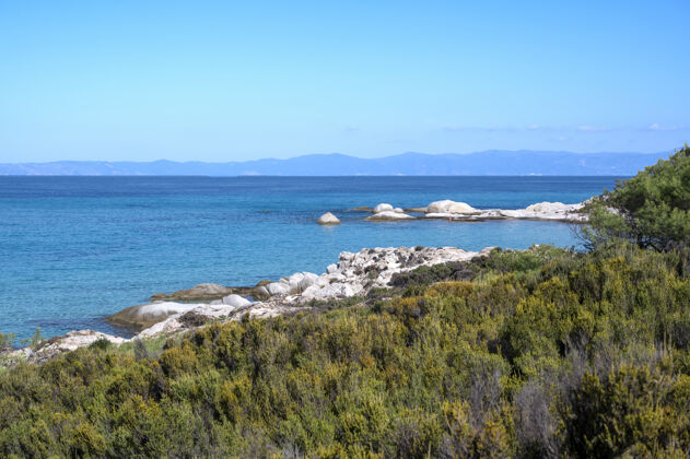 海岸爱琴海海岸 水面上有岩石 远处有陆地 前景是绿色植物 蓝色的海水 希腊爱琴海岩石悬崖