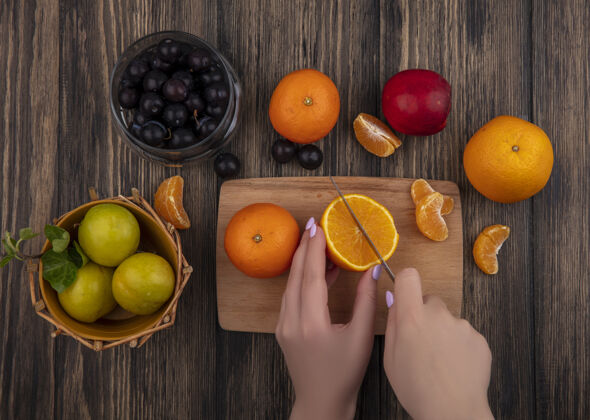 五颜六色俯视图：女人在砧板上切橘子 篮子里放着李子 木桶里放着樱桃李子板切割罐子