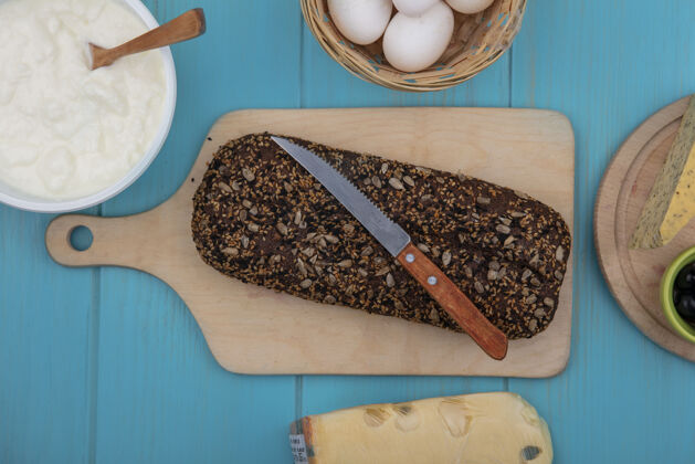 刀俯视图：黑色面包 刀子放在砧板上 鸡蛋和酸奶放在碗里 蓝绿色背景面包面包房鸡肉
