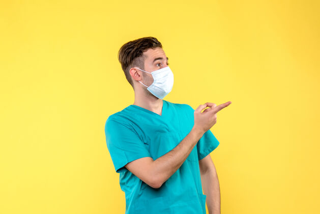 成人黄墙上戴着无菌口罩的男医生的正视图人男性医生脸