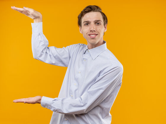 男人身穿白衬衫的年轻人面带微笑 用手展示了尺寸手势 橙色墙壁上站着测量符号显示测量看