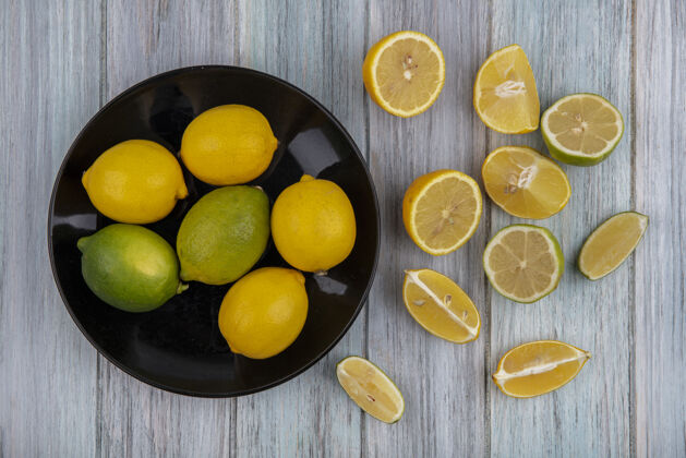 酸橙顶视图柠檬与石灰在一个黑色的板与楔在灰色的背景楔形食物顶部