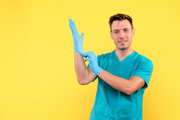 休闲黄色墙上戴着蓝色手套的男医生的正视图玩家男性医院