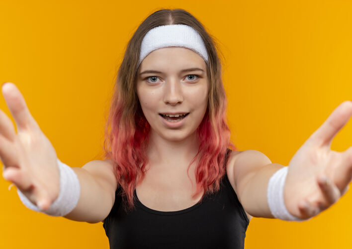 运动身着运动服的年轻健身女士站在橙色的墙上做欢迎手势欢迎运动手