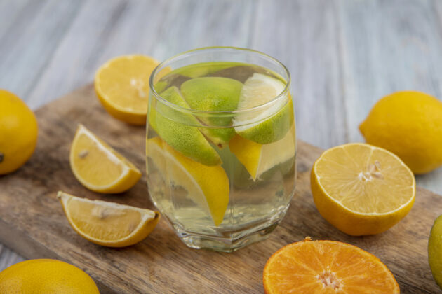 板侧视图在玻璃里用石灰楔子和半个橘子和柠檬在砧板上排毒酸橙壁板水