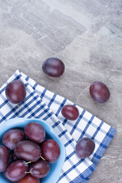 健康用桌布在石头背景上放一碗新鲜的李子紫色水果美味